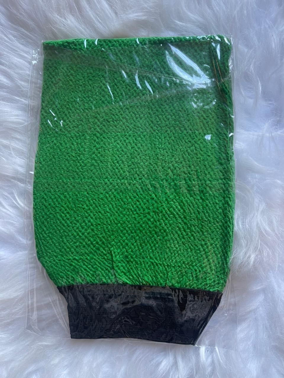 Green mesh scrubber with black base in clear packaging on a white fluffy surface