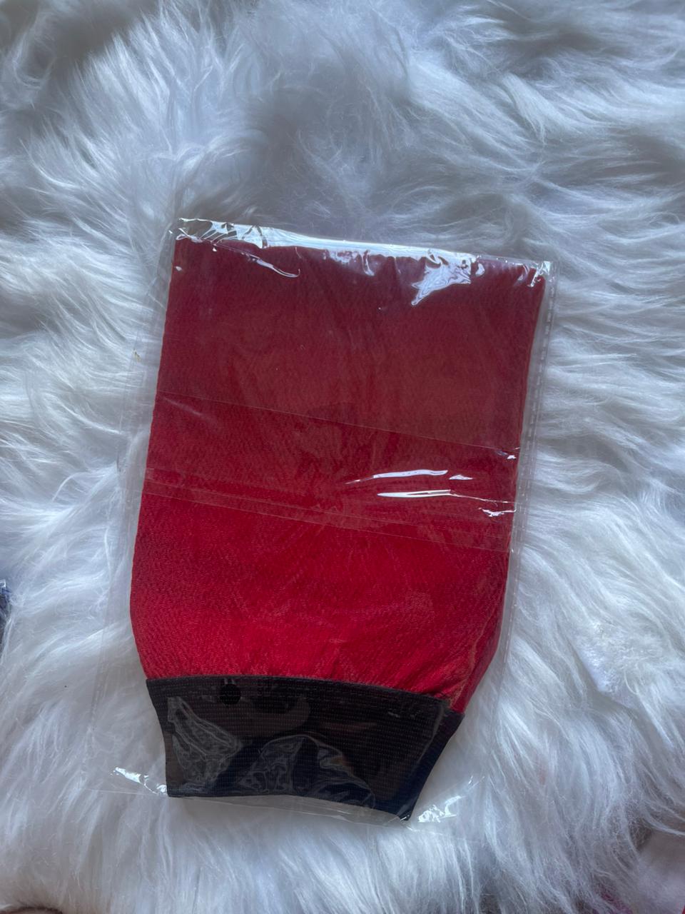 Red fabric item in clear packaging on a white furry surface